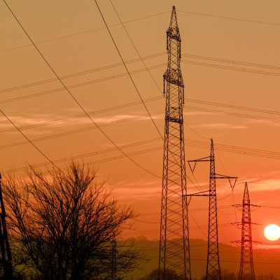 Hydropower electric voltage post against red orange sunset sky with sun low abobe horizon